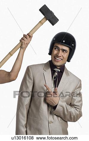 Person's hand hitting a hammer on a businessman wearing a helmet View Large Photo Image Stock Photo - Person's hand hitting a hammer on a businessman wearing a helmet. Fotosearch