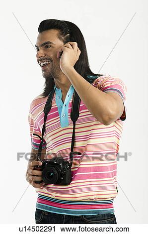 Stock Image - Photographer holding a digital camera and talking on a mobile phone. Fotosearch