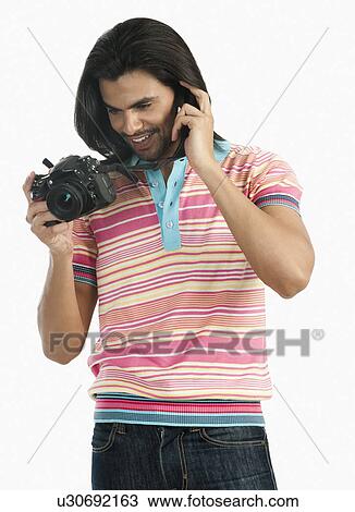 Stock Image - Photographer holding a digital camera and talking on a mobile phone. Fotosearch