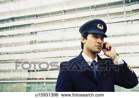Stock Photograph - Pilot talking on a mobile phone at an airport. Fotosearch