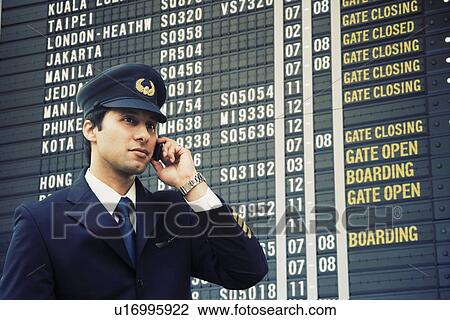 Pilot talking on a mobile phone in front of an arrival departure board at an airport View Large Photo Image Stock Image - Pilot talking on a mobile phone in front of an arrival departure board at an airport. Fotosearch