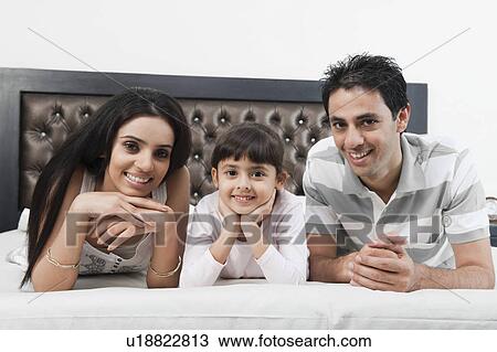 Portrait of a couple lying on the bed with their daughter View Large Photo Image Stock Image - Portrait of a couple lying on the bed with their daughter. Fotosearch