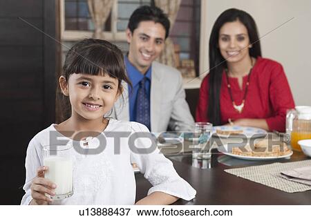 Portrait of a girl holding a glass of milk with her parents in the background View Large Photo Image Stock Photo - Portrait of a girl holding a glass of milk with her parents in the background. Fotosearch