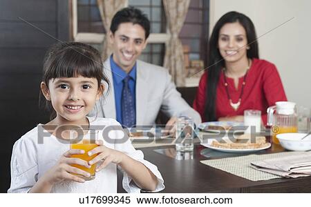 Portrait of a girl holding a glass of juice with her parents in the background View Large Photo Image Stock Photography - Portrait of a girl holding a glass of juice with her parents in the background. Fotosearch