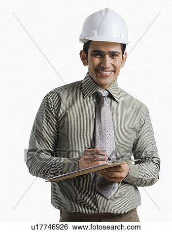 Stock Photograph - Portrait of a male engineer wearing hardhat and writing on a clipboard. Fotosearch