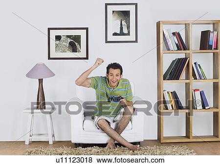 Portrait of a man cheering while playing a video game View Large Photo Image Stock Photo - Portrait of a man cheering while playing a video game. Fotosearch