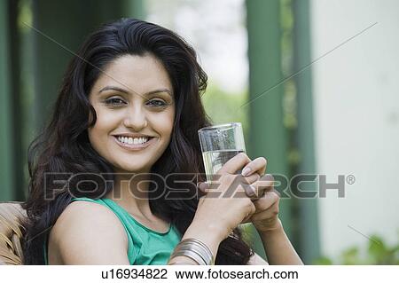 Stock Image - Portrait of a woman holding a glass of water and smiling. Fotosearch