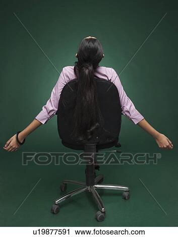 Stock Image - Rear view of a businesswoman sitting on a chair with her arm outstretched. Fotosearch