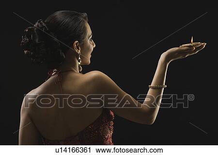Stock Image - Rear view of a woman holding an oil lamp. Fotosearch