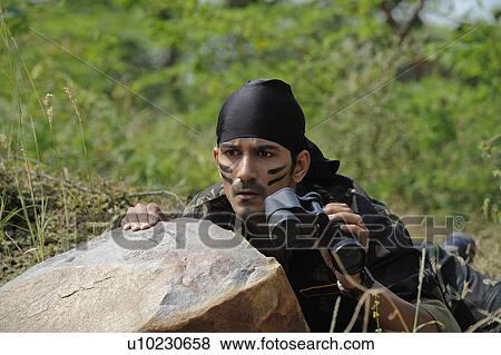 Stock Photo - Soldier hiding behind a rock with binoculars. Fotosearch
