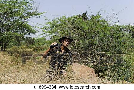 Picture - Soldier holding binoculars in a forest. Fotosearch