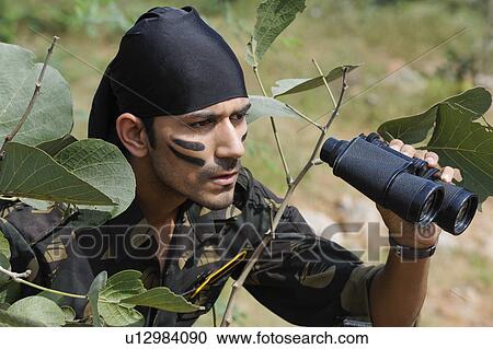 Stock Image - Soldier holding binoculars in a forest. Fotosearch