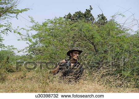 Stock Image - Soldier holding binoculars in a forest. Fotosearch