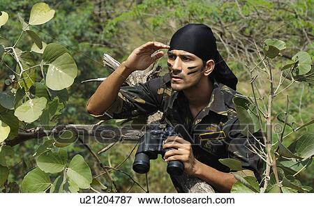 Stock Photo - Soldier holding binoculars in a forest. Fotosearch