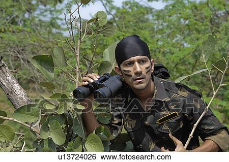 Stock Photograph - Soldier holding binoculars in a forest. Fotosearch