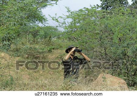 Stock Photography - Soldier looking through binoculars in a forest. Fotosearch