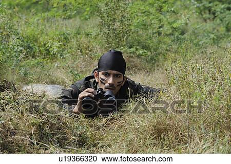 Stock Image - Soldier lying in a forest with binoculars. Fotosearch