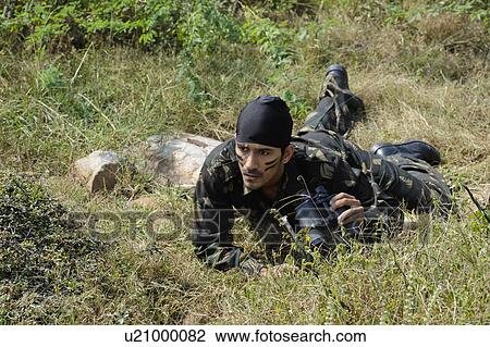 Stock Image - Soldier lying in a forest with binoculars. Fotosearch