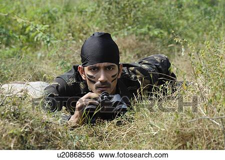 Stock Photograph - Soldier lying in a forest with binoculars. Fotosearch