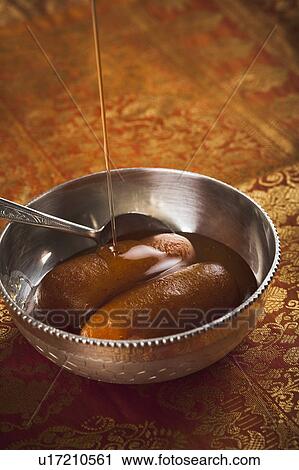 Stock Image - Sugar syrup being poured on gulab jamuns. Fotosearch