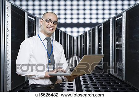 Technician working on a laptop in a server room View Large Photo Image Stock Image - Technician working on a laptop in a server room. Fotosearch