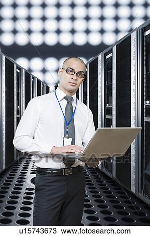 Stock Image - Technician working on a laptop in a server room. Fotosearch