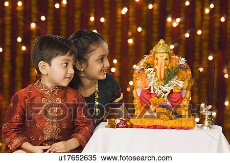Stock Photography - Two children sitting in front of the idol of lord Ganesha. Fotosearch