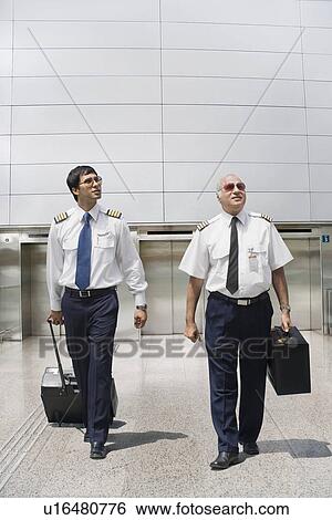 Stock Photograph - Two pilots carrying their luggage at an airport. Fotosearch