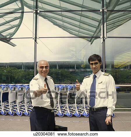 Stock Image - Two pilots showing thumbs up at an airport. Fotosearch
