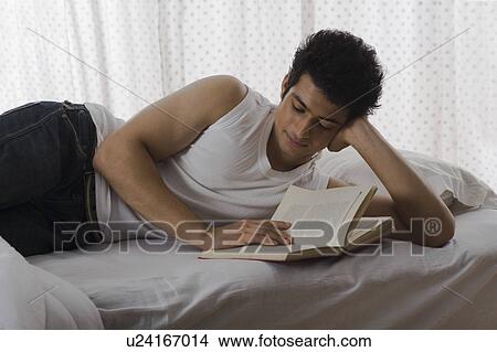 Picture - University student reading a book on the bed. Fotosearch