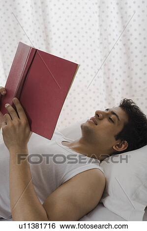 Stock Photograph - University student reading a book on the bed. Fotosearch