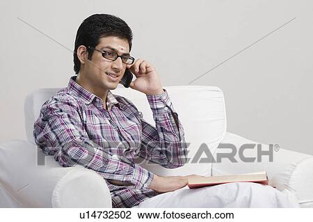 Stock Image - University student talking on a mobile phone and holding a book. Fotosearch