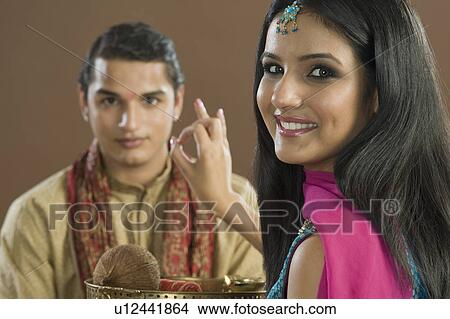 Picture - Woman applying tilak on her brother's forehead at Raksha Bandhan festival. Fotosearch