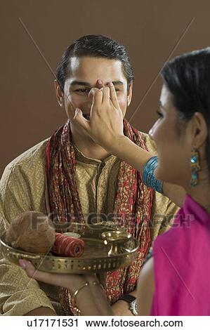 Stock Image - Woman applying tilak on her brother's forehead at Raksha Bandhan festival. Fotosearch