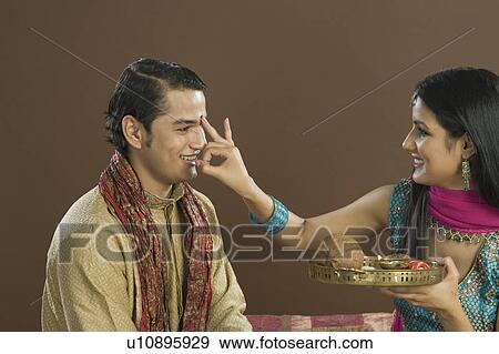 Stock Photo - Woman applying tilak on her brother's forehead at Raksha Bandhan festival. Fotosearch