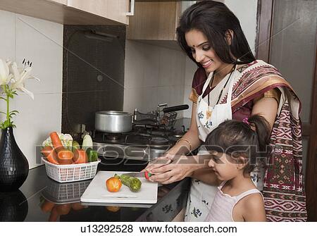 Woman chopping vegetables in the kitchen with her daughter View Large Photo Image Stock Photo - Woman chopping vegetables in the kitchen with her daughter. Fotosearch