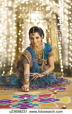Stock Image - Woman decorating oil lamps near rangoli at Diwali festival. Fotosearch