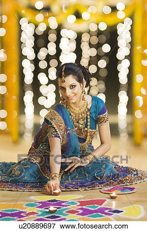Stock Photo - Woman decorating oil lamps near rangoli at Diwali festival. Fotosearch
