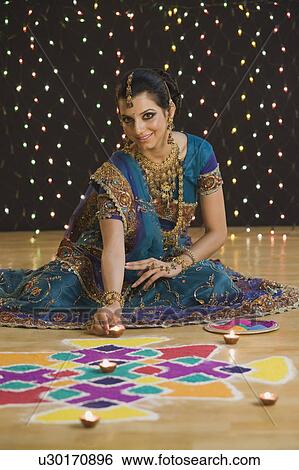Stock Photograph - Woman decorating oil lamps near rangoli at Diwali festival. Fotosearch