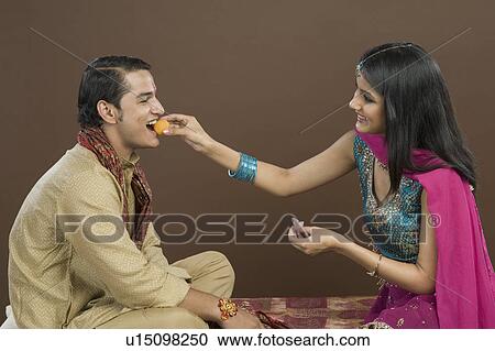 Woman feeding sweets to her brother at Raksha Bandhan festival View Large Photo Image Stock Image - Woman feeding sweets to her brother at Raksha Bandhan festival. Fotosearch