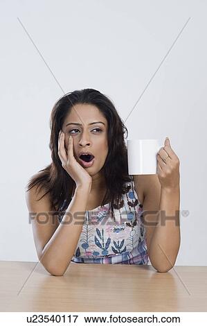 Stock Photo - Woman holding a cup of coffee and yawning. Fotosearch