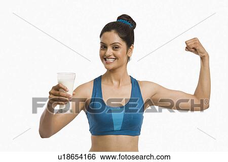 Stock Photograph - Woman holding a glass of milk and flexing her biceps. Fotosearch