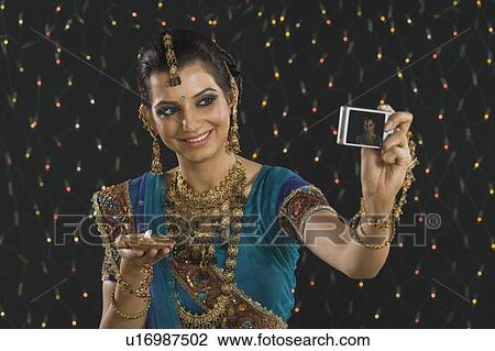 Stock Image - Woman holding an oil lamp and taking a picture of herself with a digital camera. Fotosearch