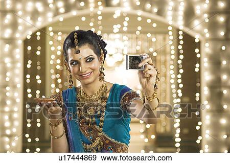 Stock Photo - Woman holding an oil lamp and taking a picture of herself with a digital camera. Fotosearch