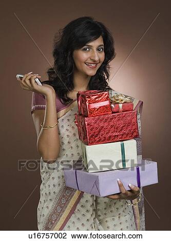 Stock Image - Woman holding mobile phone and gifts. Fotosearch