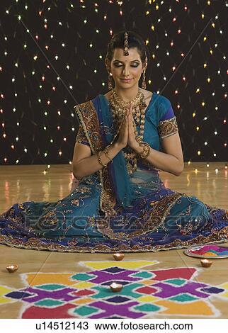 Stock Image - Woman in prayer position near rangoli at Diwali festival. Fotosearch