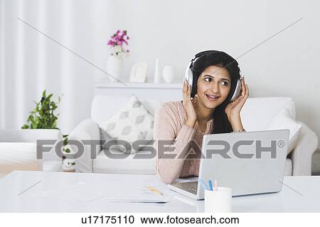 Woman listening to headphones in front of a laptop View Large Photo Image Stock Image - Woman listening to headphones in front of a laptop. Fotosearch