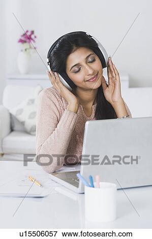 Woman listening to headphones in front of a laptop View Large Photo Image Stock Photo - Woman listening to headphones in front of a laptop. Fotosearch