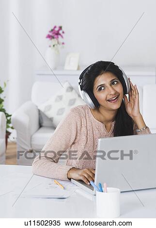 Woman listening to headphones in front of a laptop View Large Photo Image Stock Photography - Woman listening to headphones in front of a laptop. Fotosearch