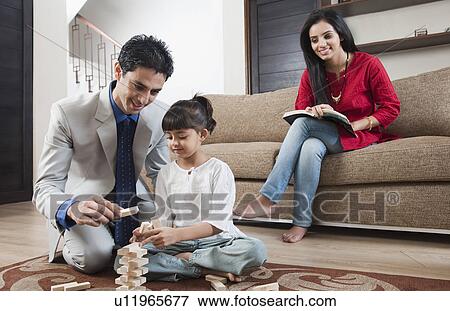 Stock Photo - Woman looking at her daughter playing Jenga with her father. Fotosearch